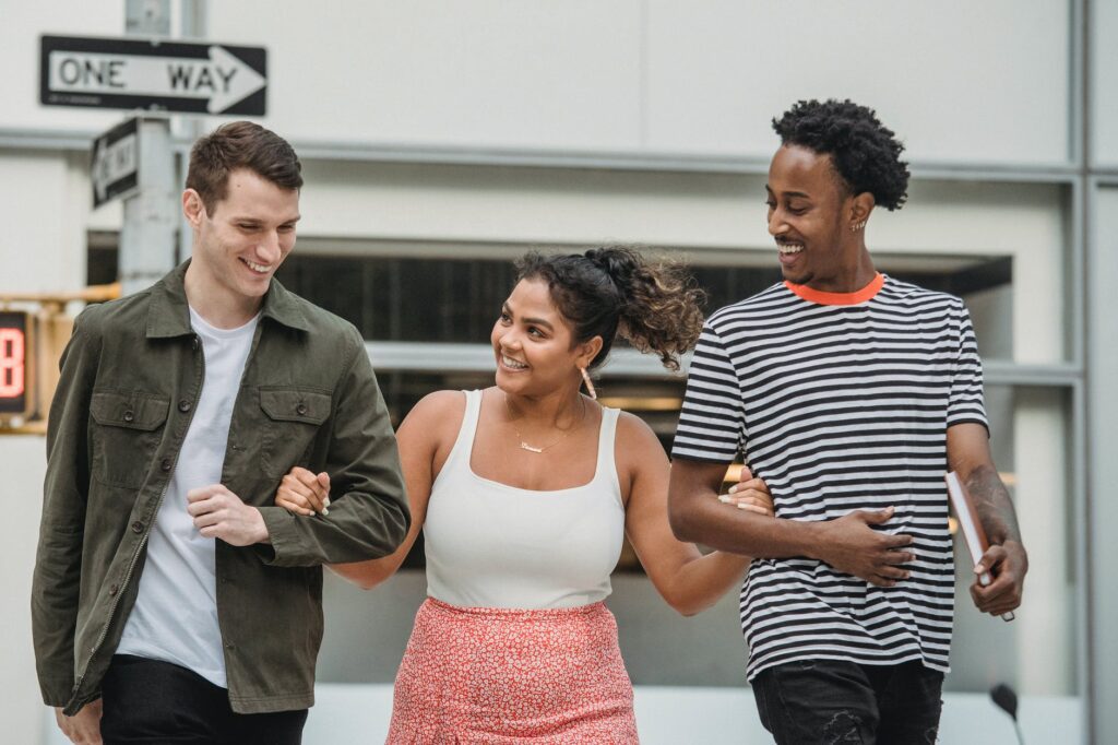 happy hispanic woman holding arms of diverse male friends while crossing road